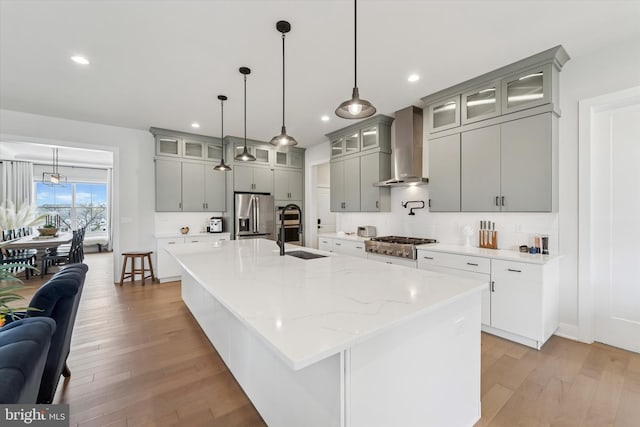 kitchen featuring gray cabinets, stainless steel appliances, light wood-type flooring, and wall chimney exhaust hood