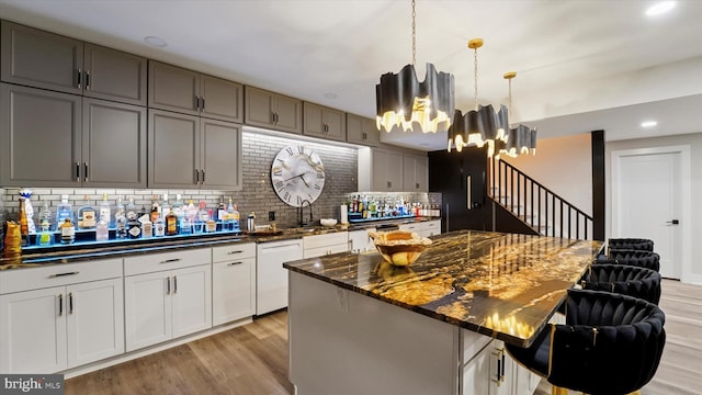 kitchen featuring light wood-type flooring, dark stone counters, tasteful backsplash, a sink, and dishwasher
