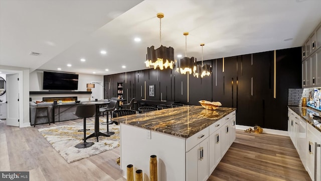 kitchen with dark stone counters, a kitchen island, wood finished floors, and white cabinetry