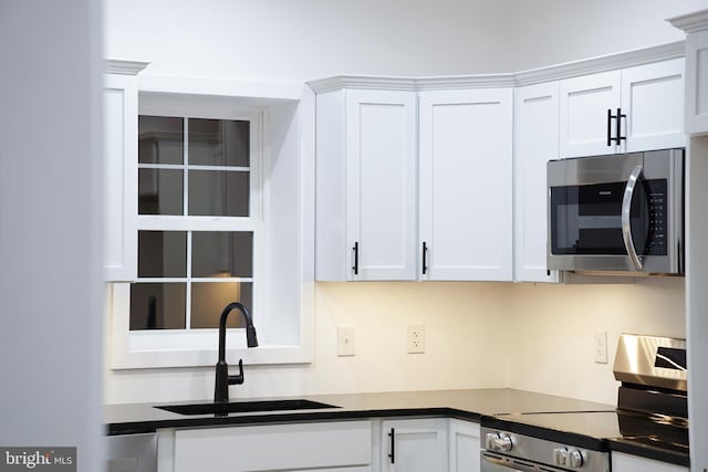 kitchen featuring a sink, appliances with stainless steel finishes, white cabinets, and dark countertops