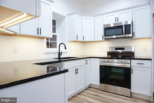 kitchen featuring dark countertops, a sink, light wood finished floors, stainless steel appliances, and white cabinetry