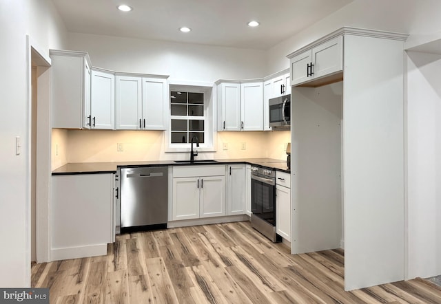 kitchen with a sink, dark countertops, stainless steel appliances, and light wood-style flooring
