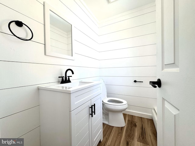 half bath featuring vanity, wood walls, wood finished floors, and toilet