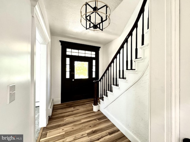 foyer entrance with baseboards, a notable chandelier, wood finished floors, and stairway