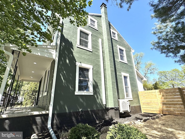 view of side of property with stucco siding, fence, ac unit, and a chimney