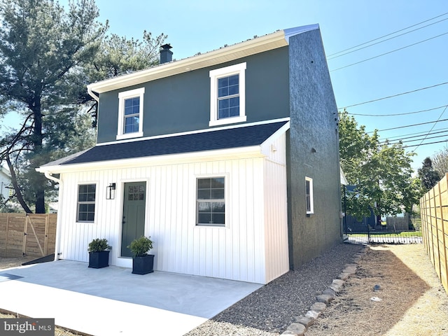 view of front of property with board and batten siding, a patio, fence, and a chimney