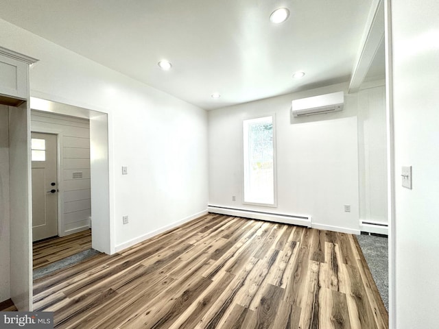 unfurnished room featuring baseboards, a baseboard radiator, a wall mounted AC, and wood finished floors
