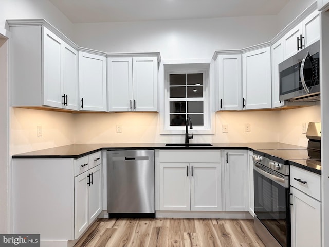 kitchen featuring dark countertops, a sink, light wood-style flooring, stainless steel appliances, and white cabinetry