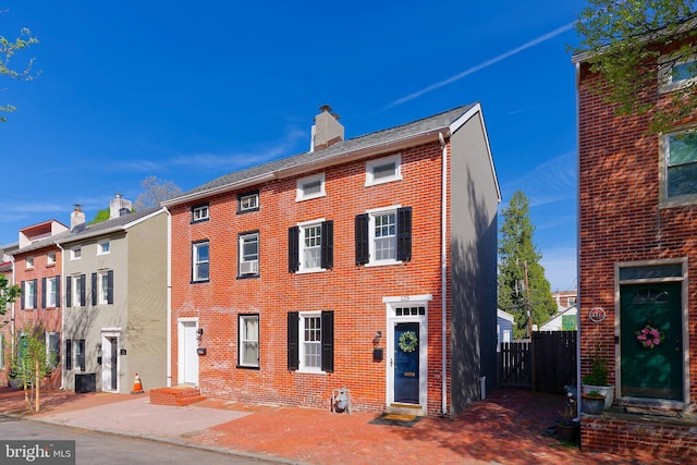 view of front of property featuring brick siding, fence, a chimney, and entry steps