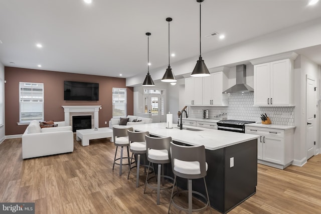 kitchen with wall chimney range hood, decorative backsplash, a sink, stainless steel range with gas cooktop, and white cabinetry