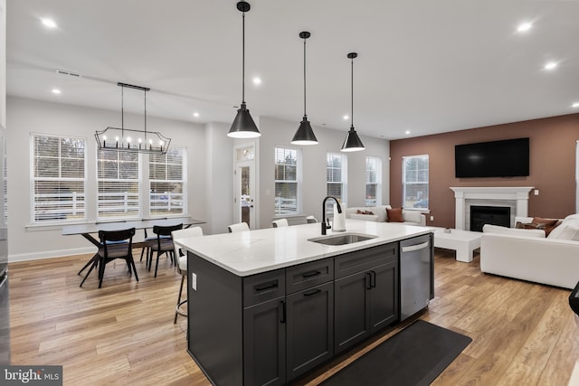 kitchen with stainless steel dishwasher, a fireplace, a sink, recessed lighting, and light wood-style flooring