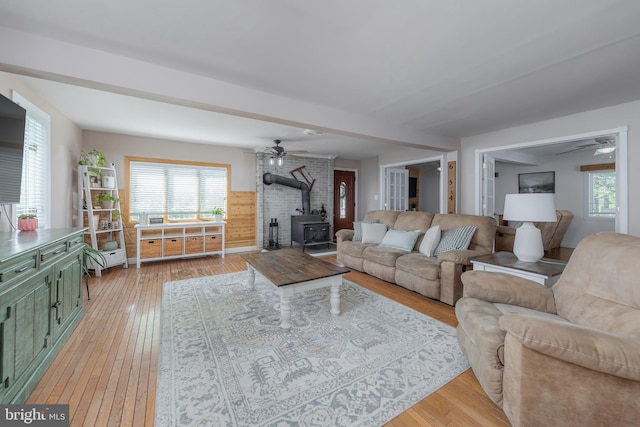 living area featuring a ceiling fan, a wood stove, and light wood-style flooring