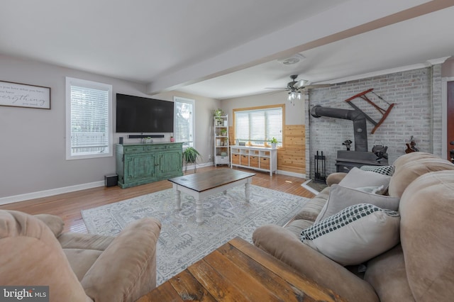 living area featuring baseboards, ceiling fan, wood finished floors, and a wood stove
