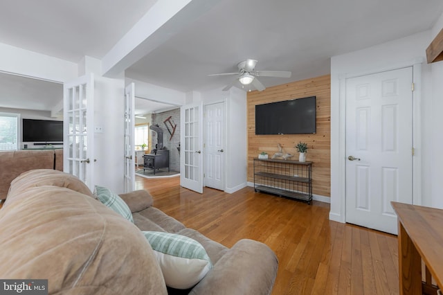 living room with french doors, wood walls, a ceiling fan, and wood finished floors