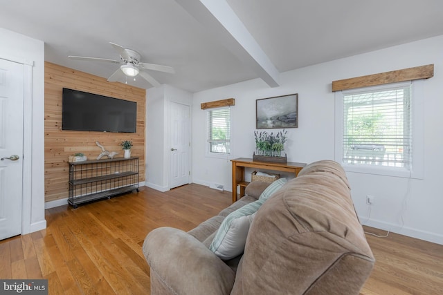 living room with baseboards, ceiling fan, wood walls, and wood finished floors
