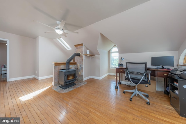 office area with ceiling fan, a wood stove, light wood-type flooring, baseboards, and lofted ceiling