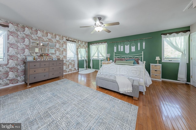 bedroom with multiple windows, wallpapered walls, and hardwood / wood-style floors