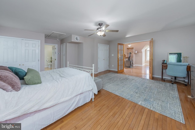 bedroom with multiple closets, hardwood / wood-style floors, baseboards, attic access, and a ceiling fan