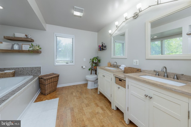 bathroom featuring vanity, toilet, baseboards, wood finished floors, and a bath
