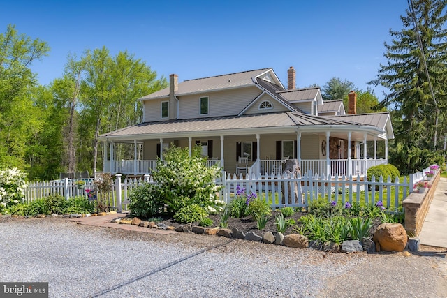 farmhouse-style home with covered porch, fence, a chimney, and metal roof