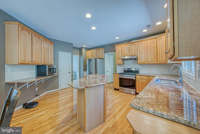 kitchen featuring light stone countertops, light wood-type flooring, a sink, under cabinet range hood, and stainless steel appliances
