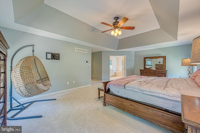 carpeted bedroom with a ceiling fan, visible vents, baseboards, connected bathroom, and a tray ceiling