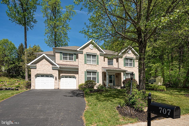 colonial home with brick siding, an attached garage, aphalt driveway, and a front yard