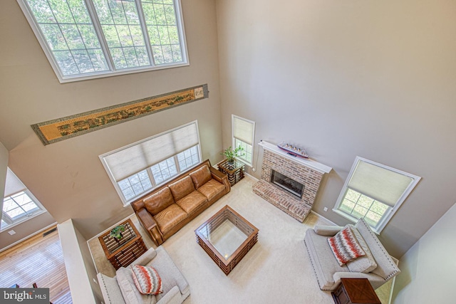 living area with carpet, a brick fireplace, and a towering ceiling