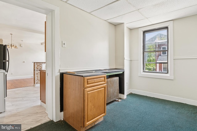 kitchen featuring baseboards, freestanding refrigerator, a notable chandelier, radiator heating unit, and a drop ceiling