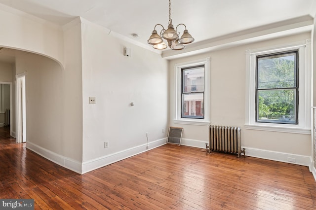 unfurnished dining area featuring an inviting chandelier, wood-type flooring, arched walkways, radiator, and baseboards