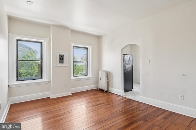 empty room with wood-type flooring, arched walkways, baseboards, and radiator heating unit