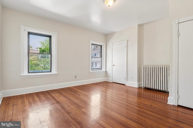 spare room featuring baseboards, radiator heating unit, and hardwood / wood-style flooring