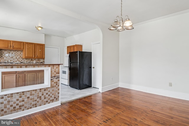 kitchen with brown cabinetry, freestanding refrigerator, decorative backsplash, hardwood / wood-style floors, and arched walkways