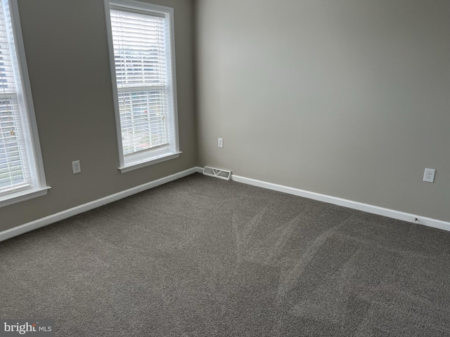 empty room with a healthy amount of sunlight, baseboards, dark colored carpet, and visible vents