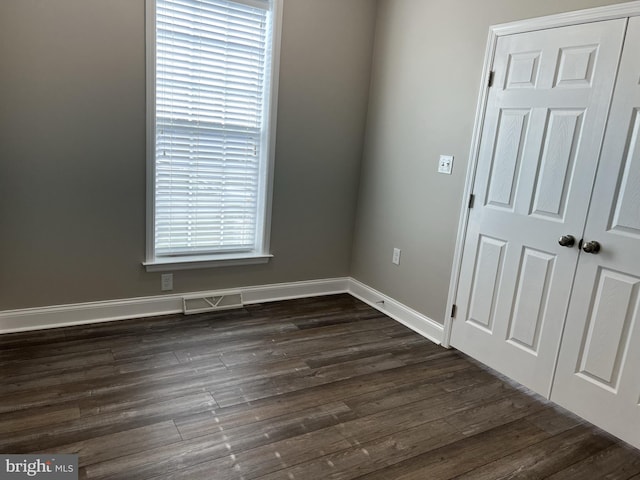 empty room featuring baseboards, dark wood-style floors, and visible vents