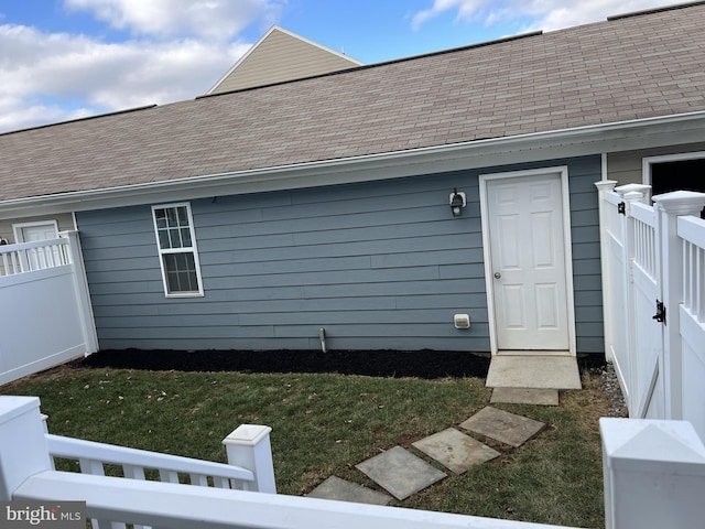 doorway to property with a lawn, fence, and roof with shingles
