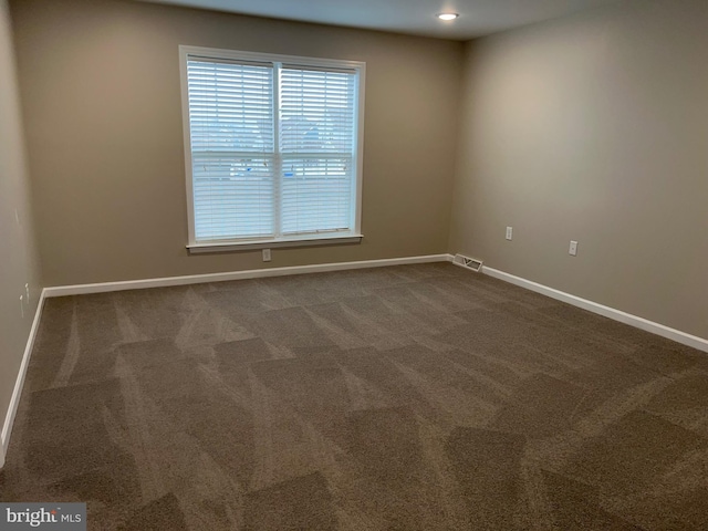 empty room with baseboards, dark colored carpet, and visible vents