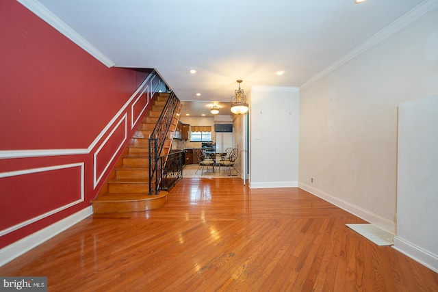 living area with ornamental molding, light wood finished floors, and stairway