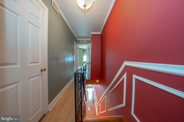 corridor with visible vents, crown molding, wood finished floors, baseboards, and an upstairs landing