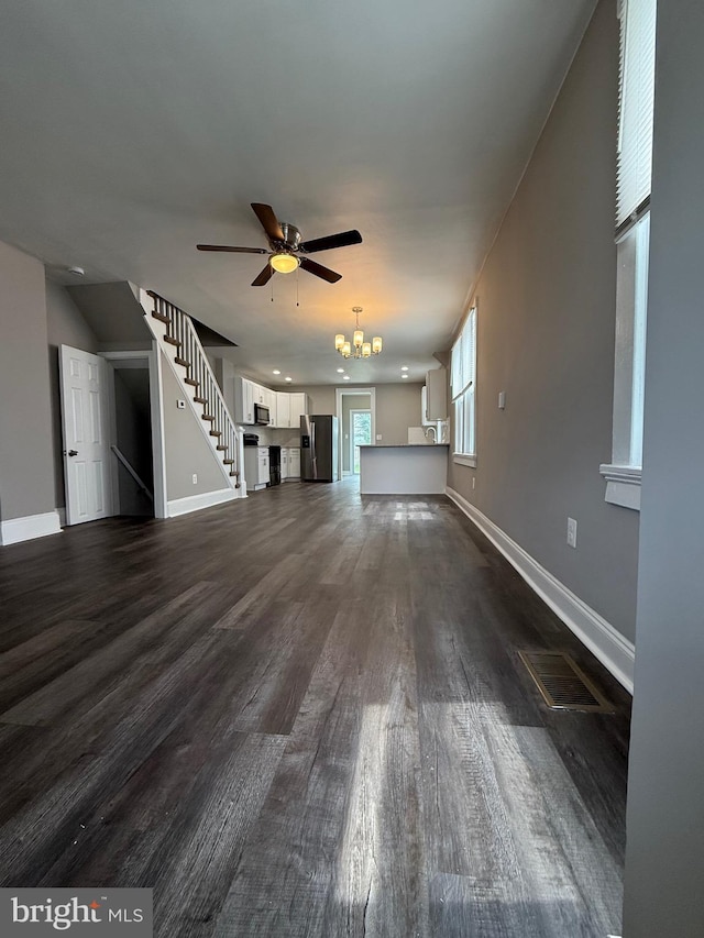 unfurnished living room featuring baseboards, dark wood-style flooring, ceiling fan with notable chandelier, and visible vents