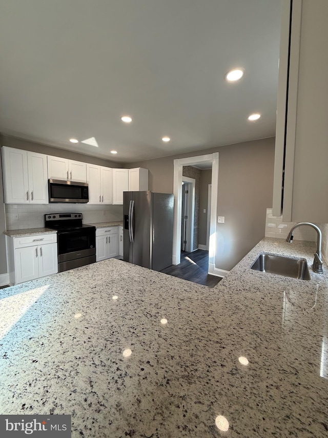 kitchen featuring backsplash, a sink, light stone counters, stainless steel appliances, and white cabinetry