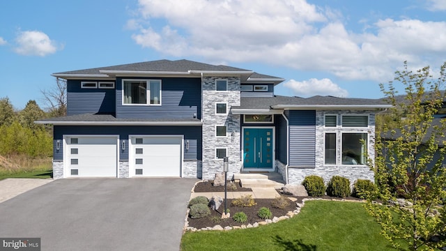 prairie-style home with an attached garage, a front lawn, stone siding, and aphalt driveway