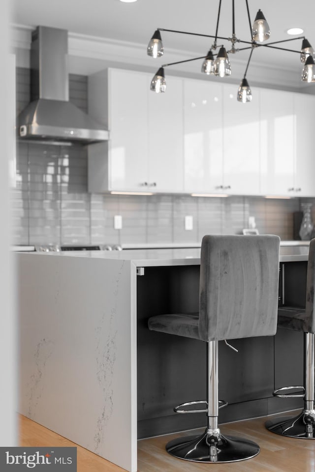 kitchen featuring wall chimney range hood, white cabinetry, light wood-style flooring, and backsplash