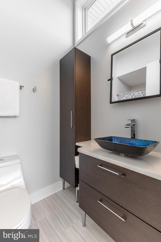 half bathroom with vanity, baseboards, and toilet