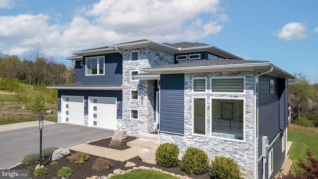 view of front of house featuring an attached garage, driveway, and stone siding