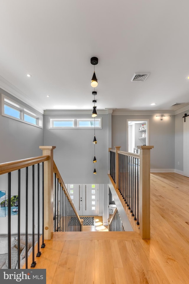 corridor featuring crown molding, visible vents, wood finished floors, and an upstairs landing