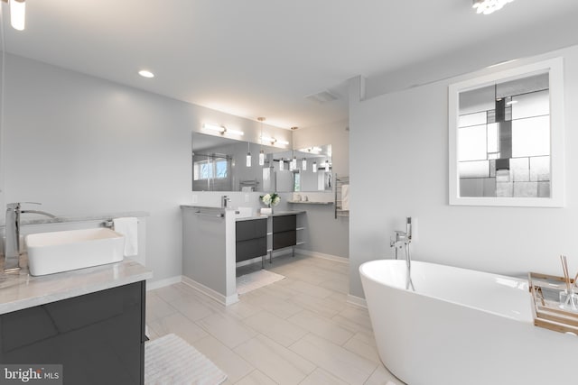 full bathroom with double vanity, a freestanding tub, a sink, baseboards, and recessed lighting