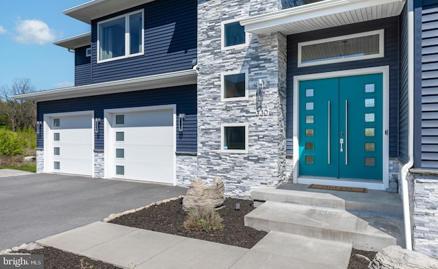 doorway to property with a garage, driveway, and stone siding
