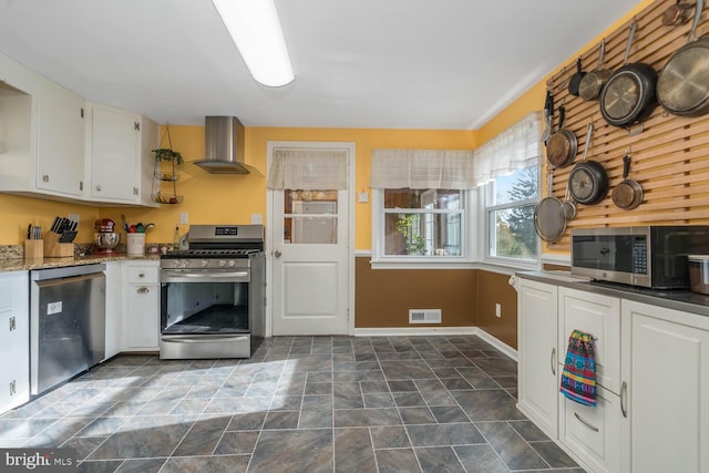 kitchen featuring visible vents, stone finish floor, wall chimney exhaust hood, white cabinets, and stainless steel appliances