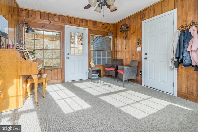 carpeted entrance foyer with ceiling fan and wood walls